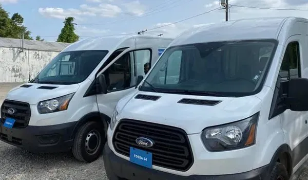 Two white Ford Transit vans parked outside, under a blue sky.