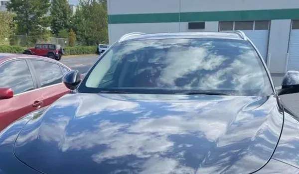 Black car with cloudy sky reflecting on the hood and windshield, parked outdoors.