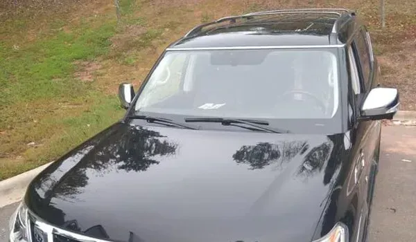 Black SUV parked on grass, reflecting trees in the hood.