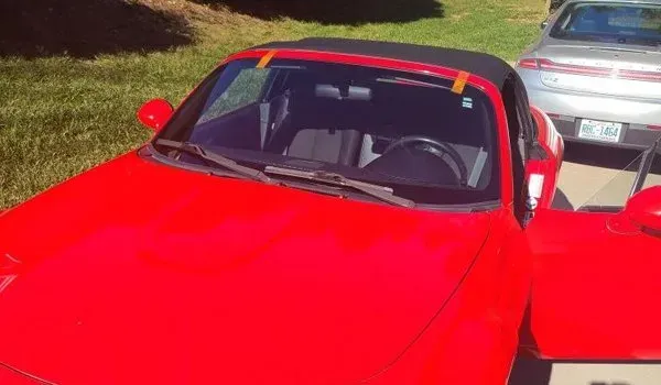 Red convertible car with an open door in a sunny outdoor setting.