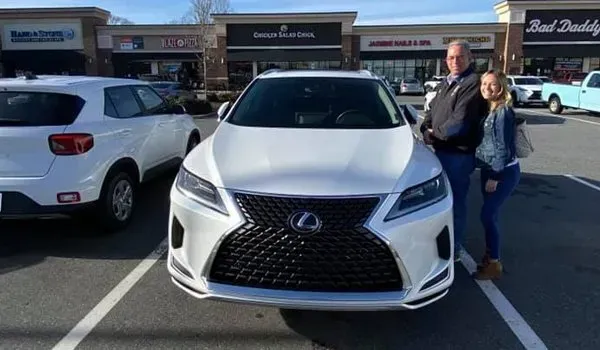 Man and woman stand beside a white Lexus SUV in a parking lot.