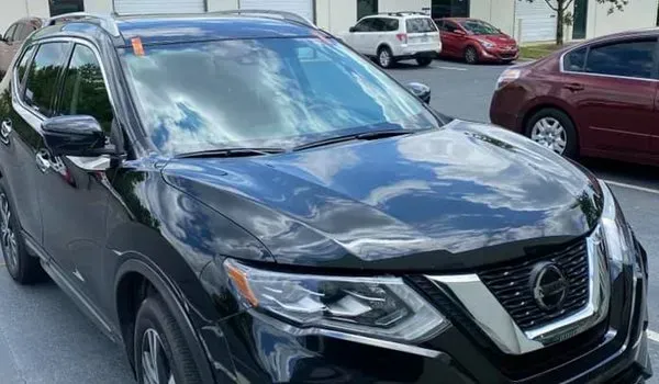 Black Nissan Rogue SUV parked in a lot with other vehicles in the background.