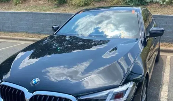 Black BMW sedan parked in a parking lot; the hood reflects a cloudy sky.