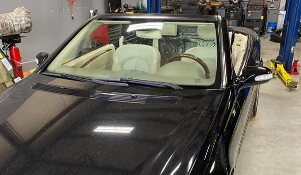 Black convertible car with tan interior in a repair shop.