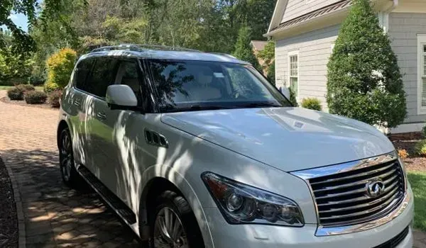 White Infiniti QX80 SUV parked on a driveway in front of a house on a sunny day.