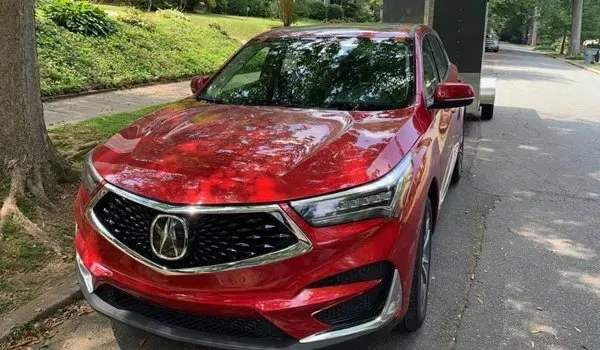Red Acura SUV parked on a residential street next to a tree, with a trailer hitched to it.