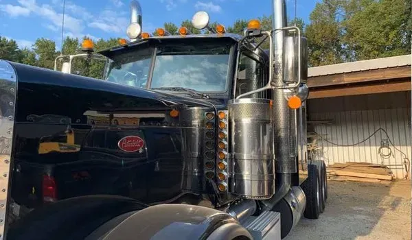 Black Peterbilt semi-truck with chrome details, parked outside on a sunny day.