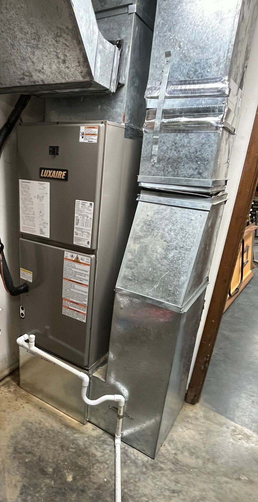 Silver HVAC unit with attached ductwork in a basement setting.