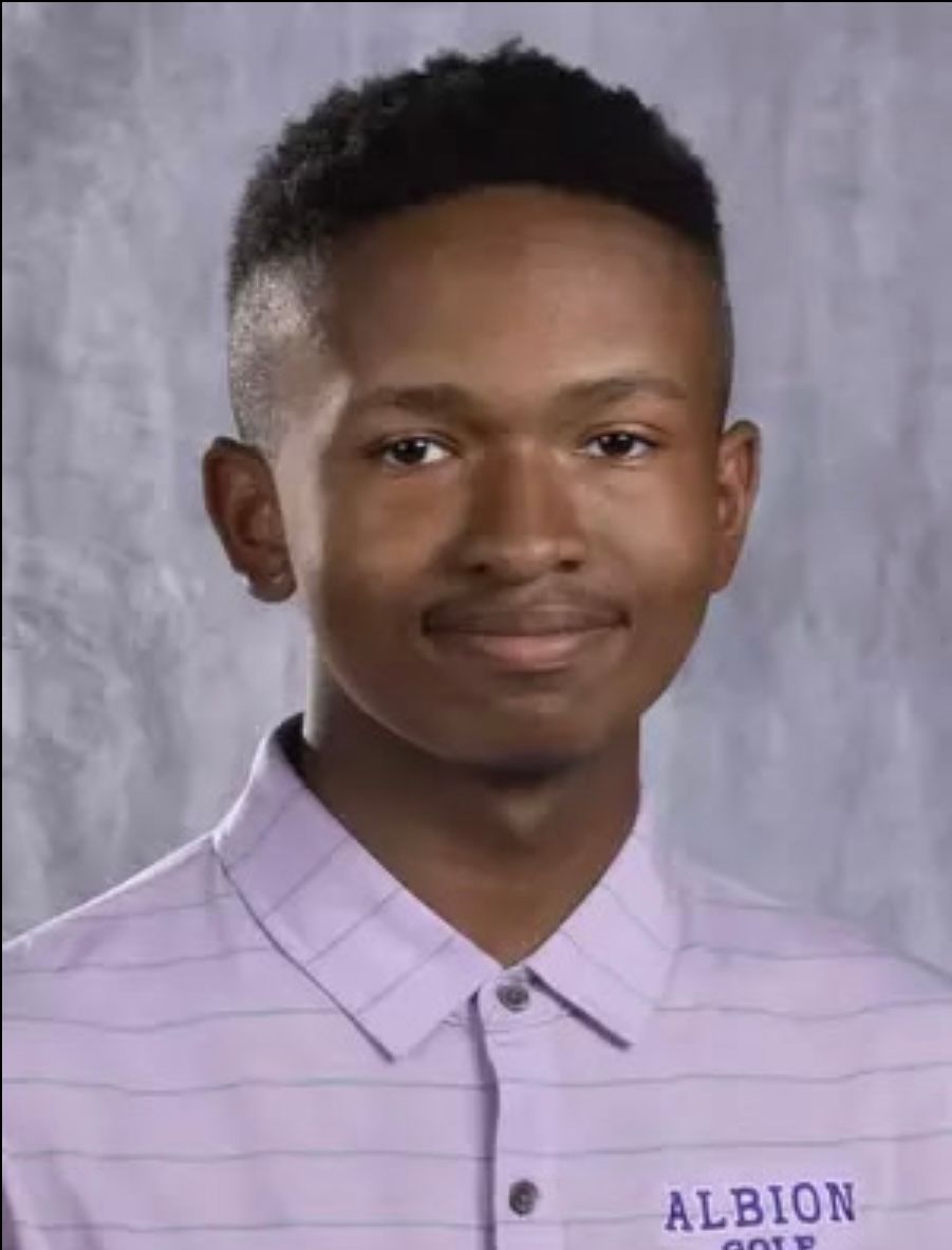Young person in a purple collared shirt smiling, with “ALBION GOLF” on the shirt.