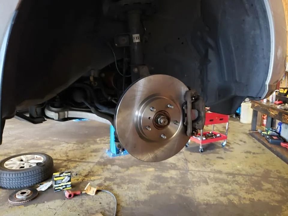 Car wheel assembly with new brake rotor, tire, and tools in a garage.