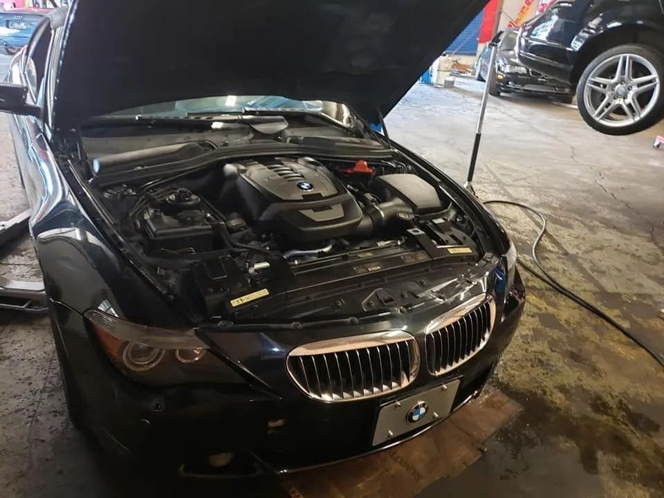 Black BMW with hood open in a garage, showing engine components.
