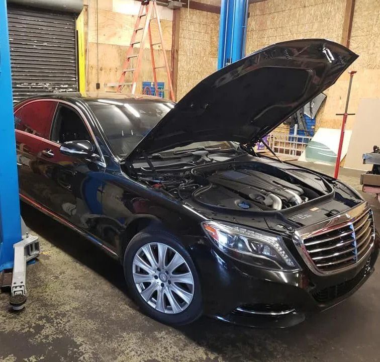 Black Mercedes-Benz sedan with hood open in an auto repair shop.
