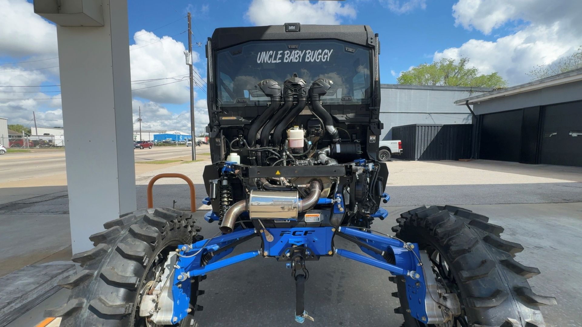 A customized black off-road vehicle with large treaded tires and blue suspension, parked in an outdoor lot.