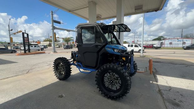 A blue and black off-road utility vehicle with oversized mud tires parked under a gas station canopy.