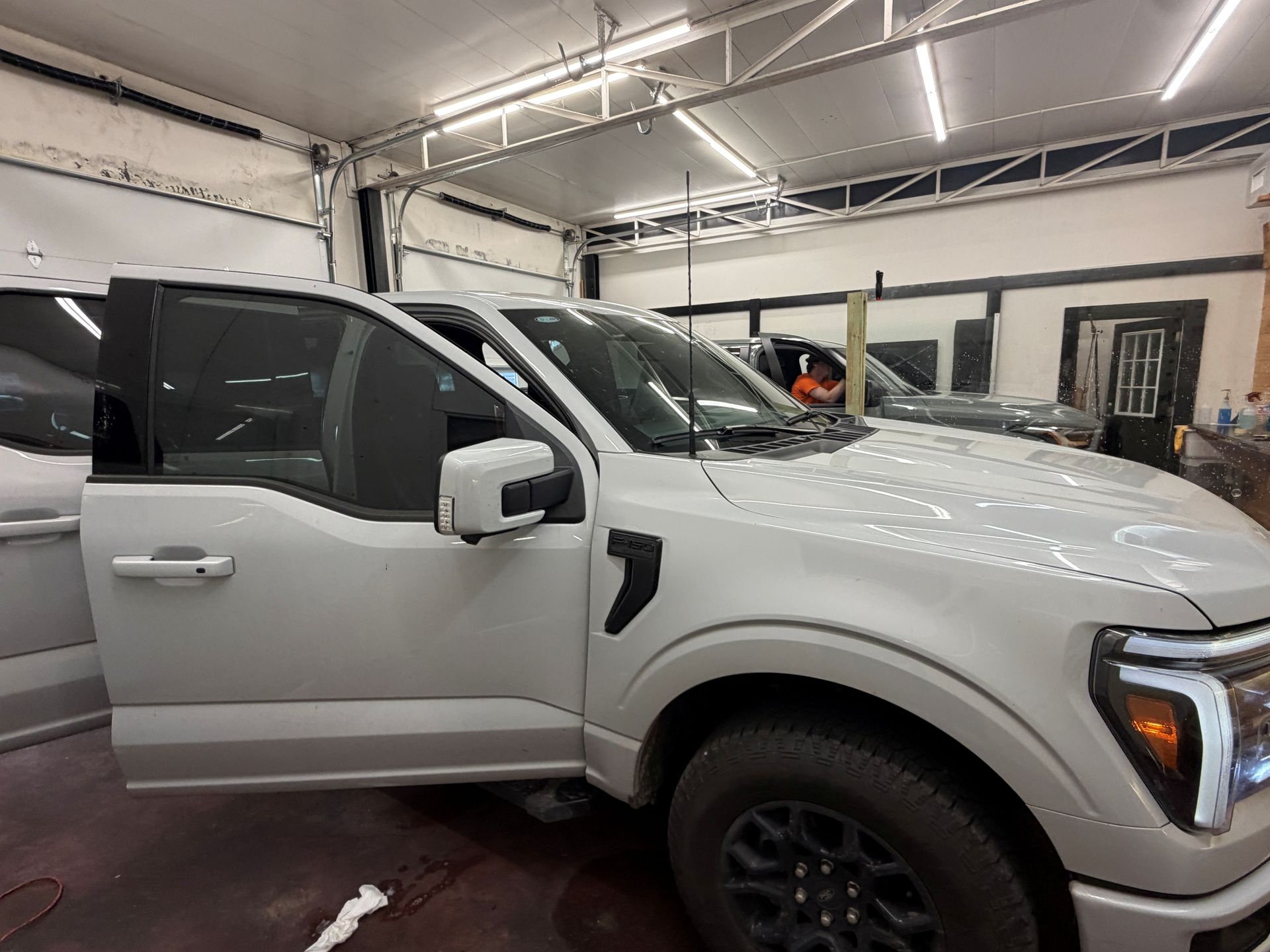 A light-colored pickup truck with an open driver's side door parked inside a well-lit automotive workshop.