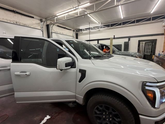 A light-colored Ford F-150 truck with its driver-side door open inside a well-lit auto shop.