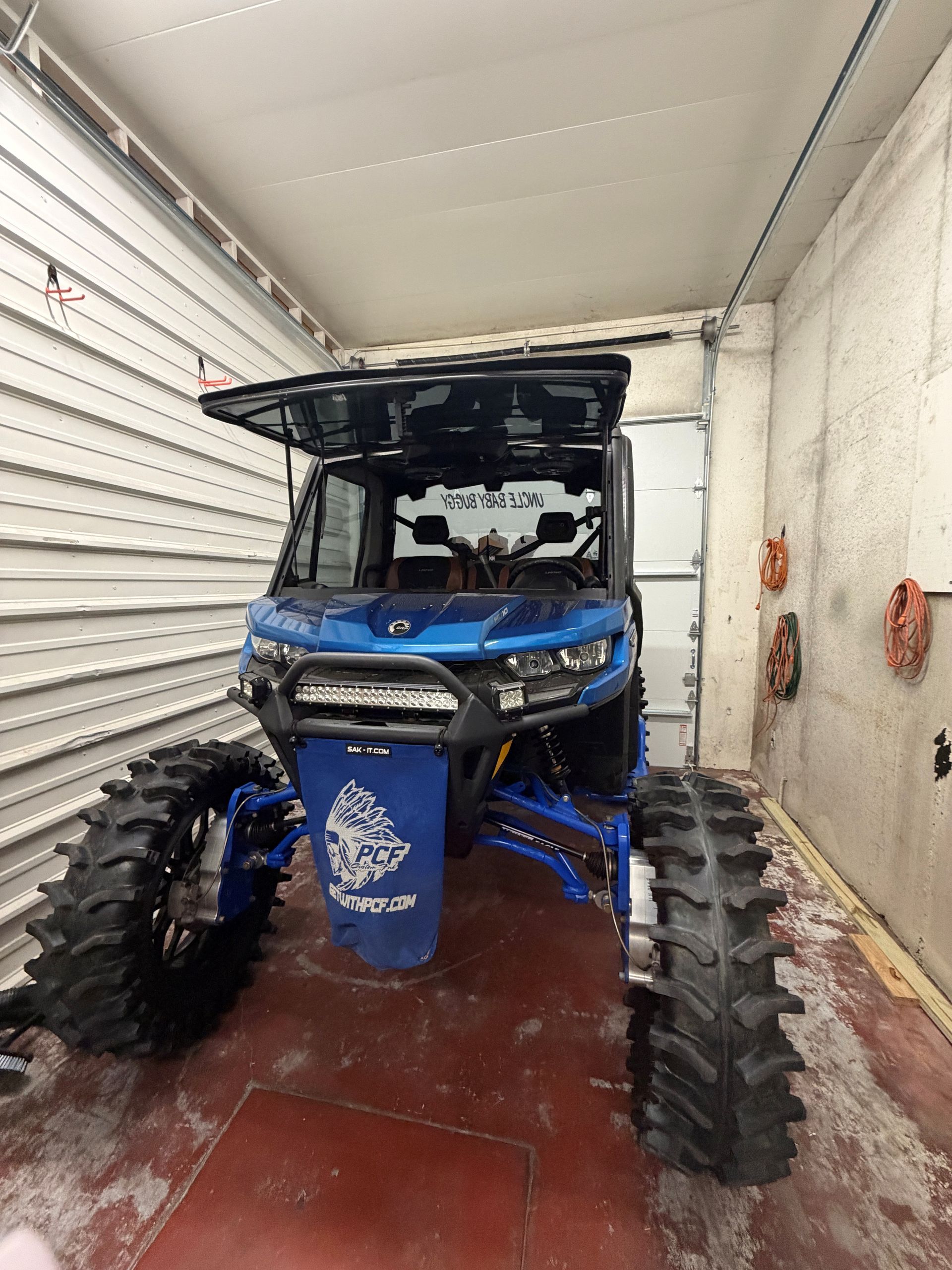 A blue side-by-side off-road vehicle with large mud tires and a roof parked in a garage.