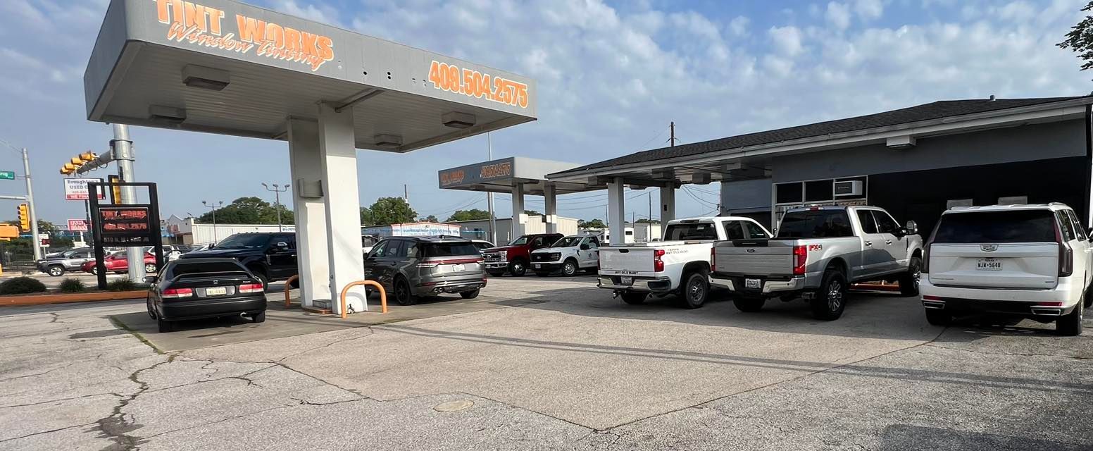 A car wash facility with covered bays and several vehicles parked on a gravel lot under a bright, sunny sky.