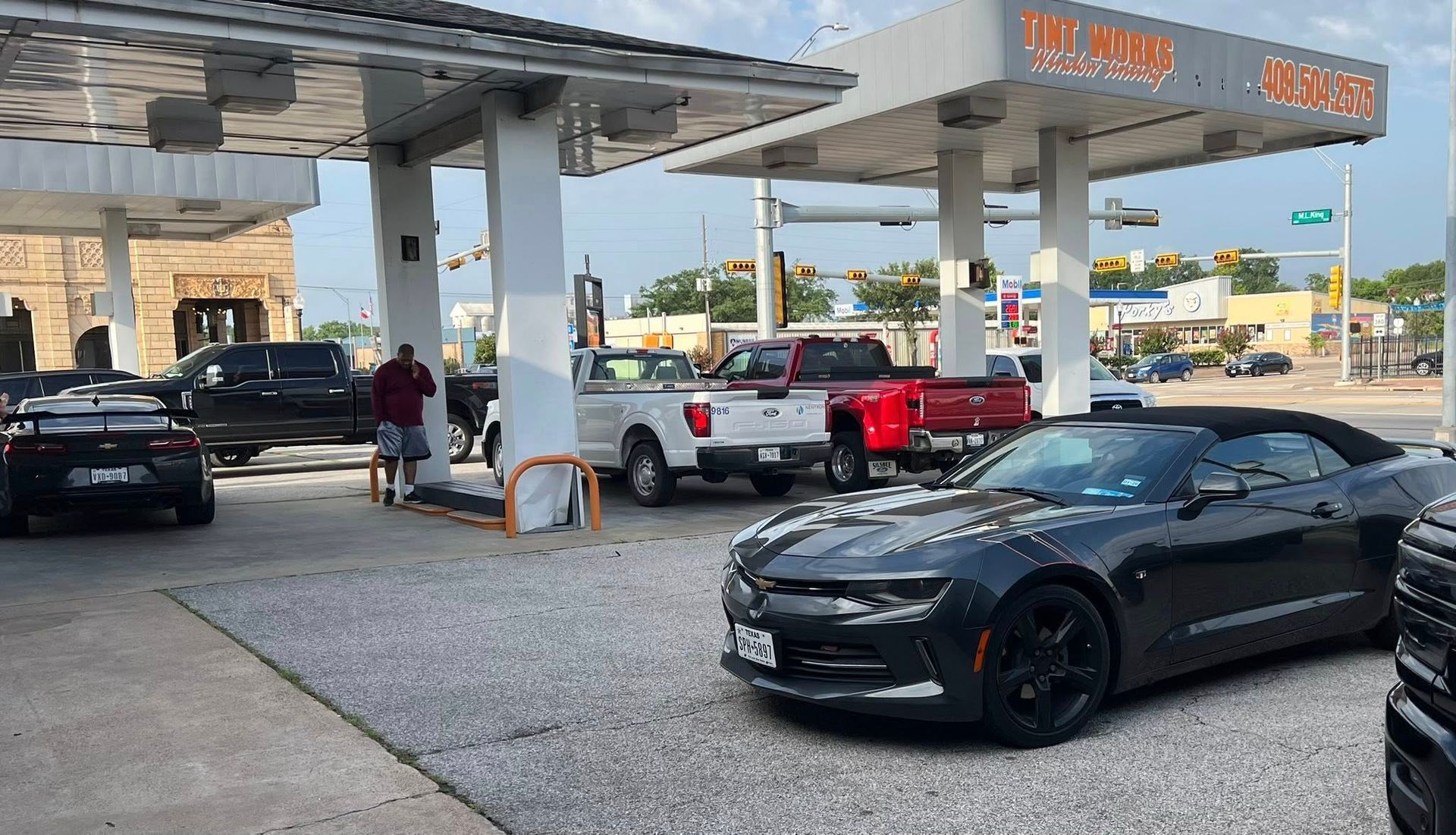 A black convertible and other vehicles parked at a gas station during the day.