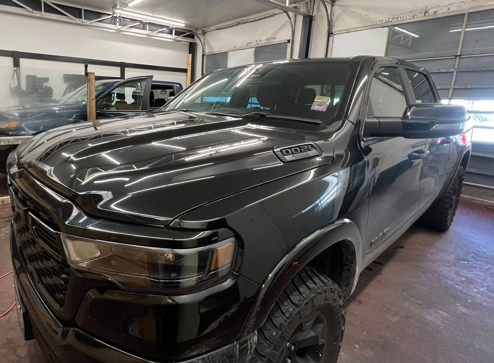 A dark, modern Ram pickup truck parked inside a garage, angled toward the viewer with headlights visible.