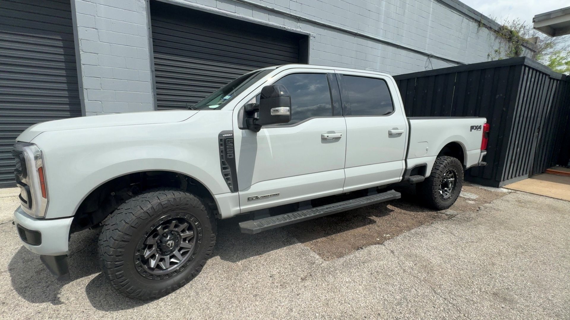 Light gray Ford F-250 pickup truck parked on gravel in front of a building with dark-colored siding.