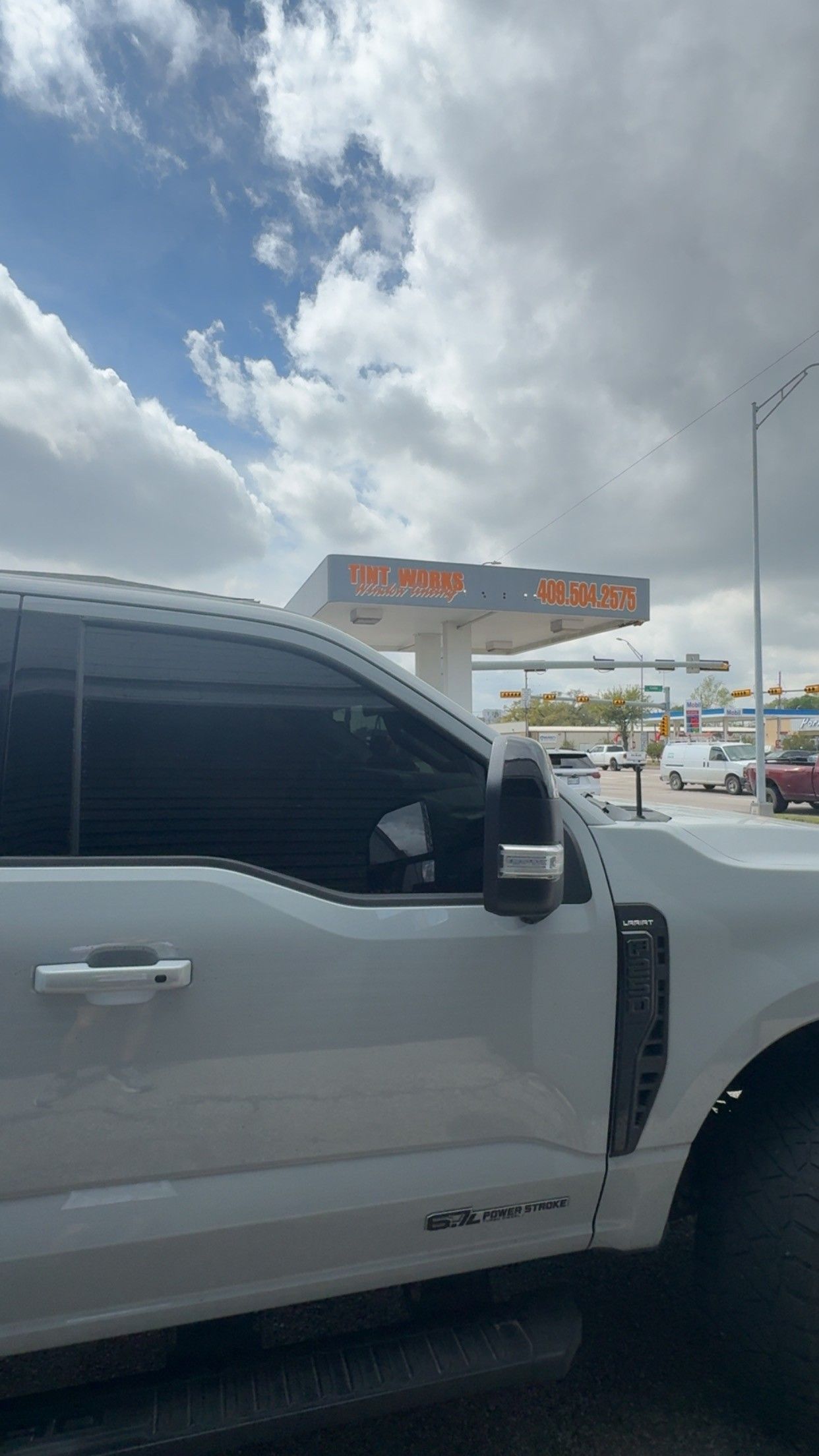 A close-up view of the side of a white pickup truck parked at a gas station under a cloudy sky.