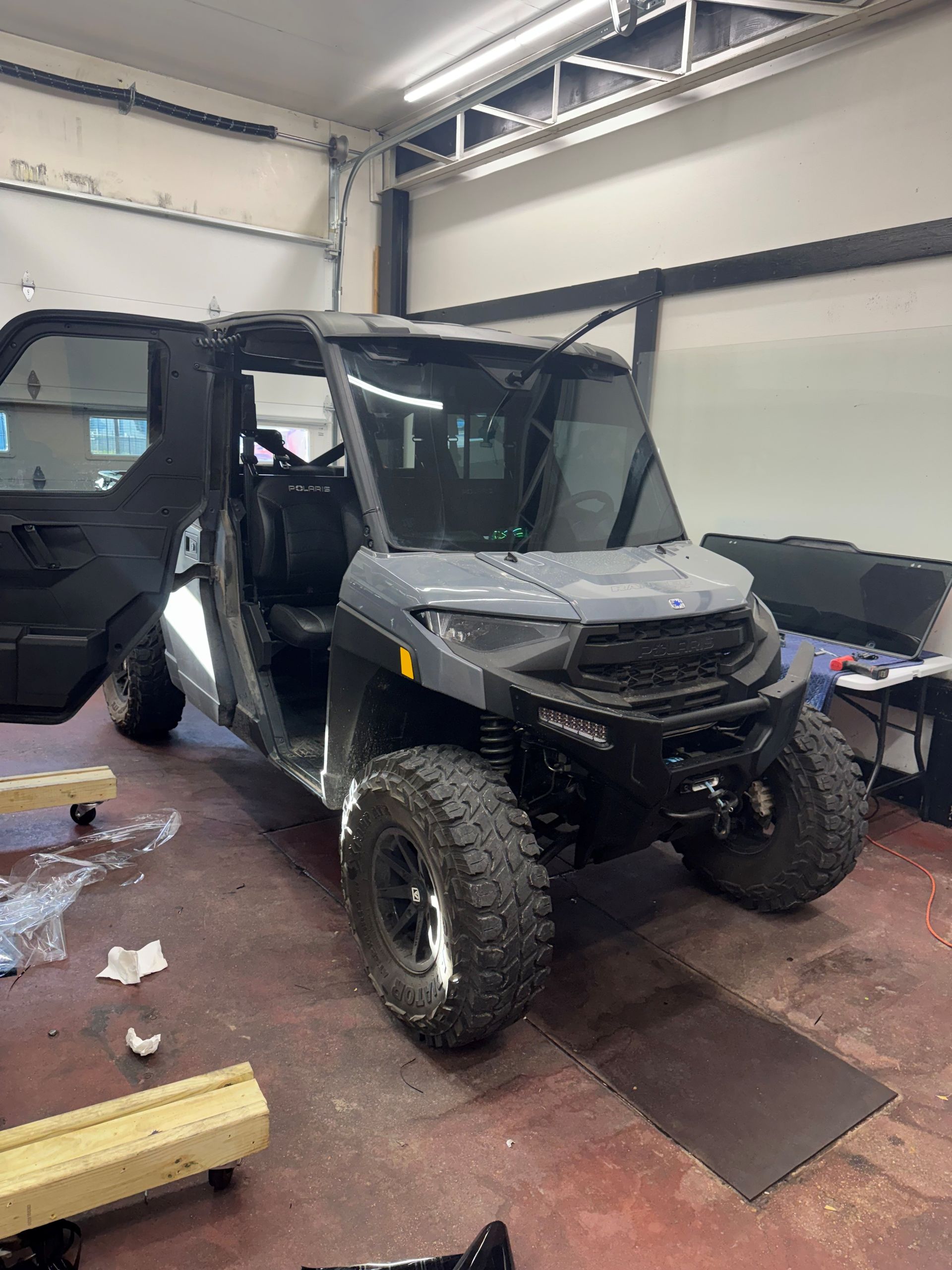 A gray Polaris Ranger UTV parked inside a garage with the driver-side door open.