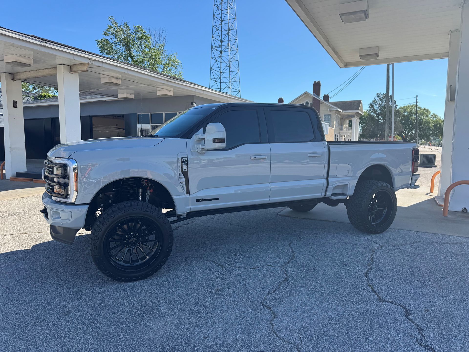 A light grey Ford F-Series crew cab pickup truck parked at a gas station on a sunny day.