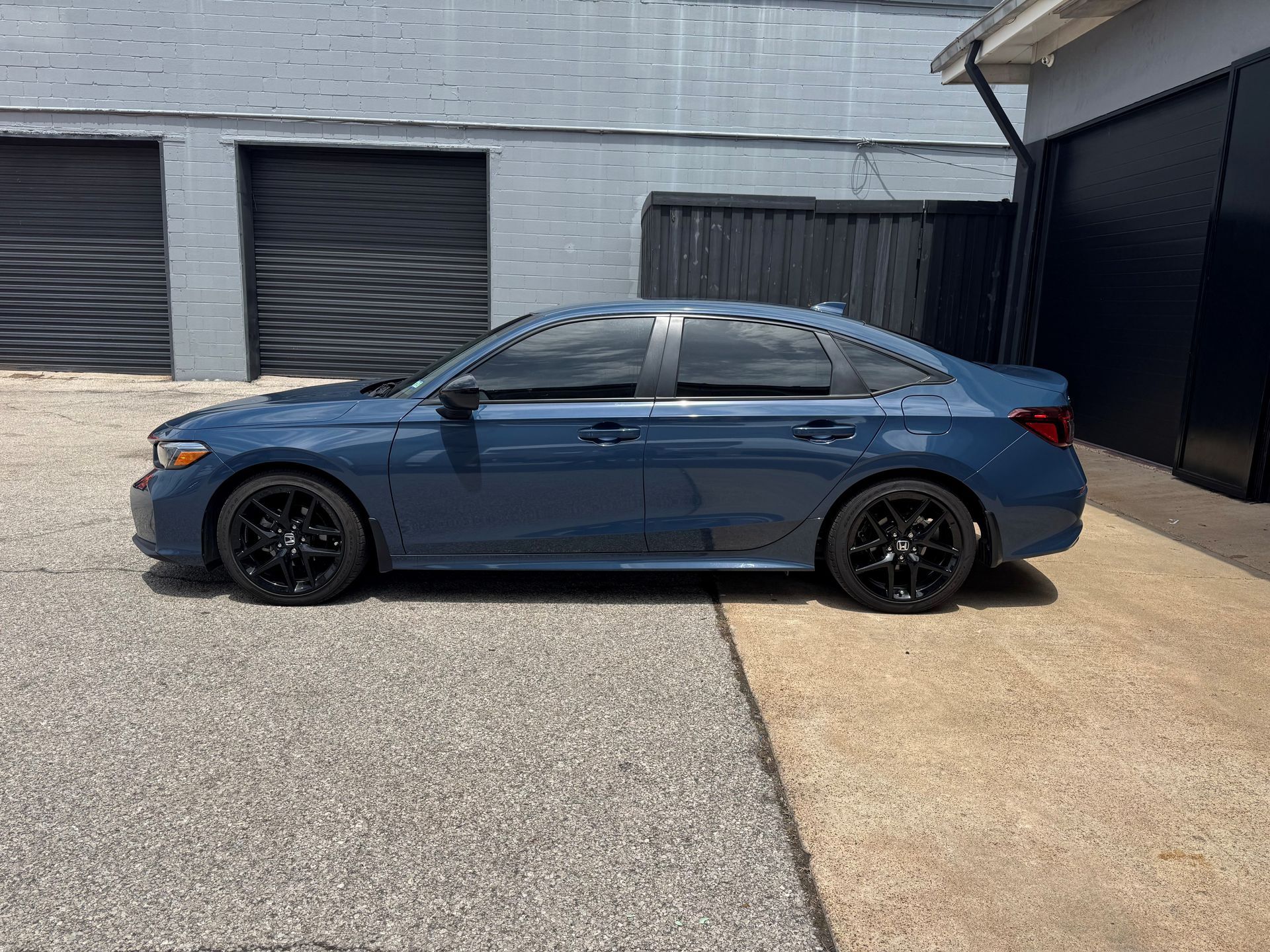 Blue sedan parked beside a black garage in a driveway.