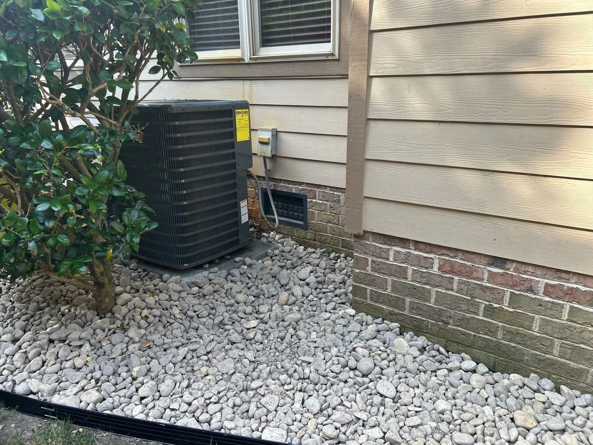 An air conditioning unit next to a house with pebble landscaping.
