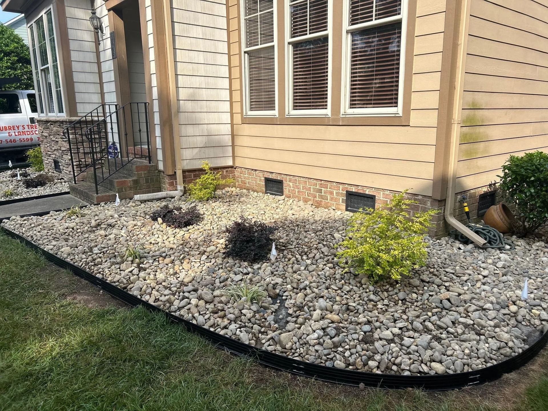 A house with a gravel bed, plants, and black edging along the foundation and lawn.