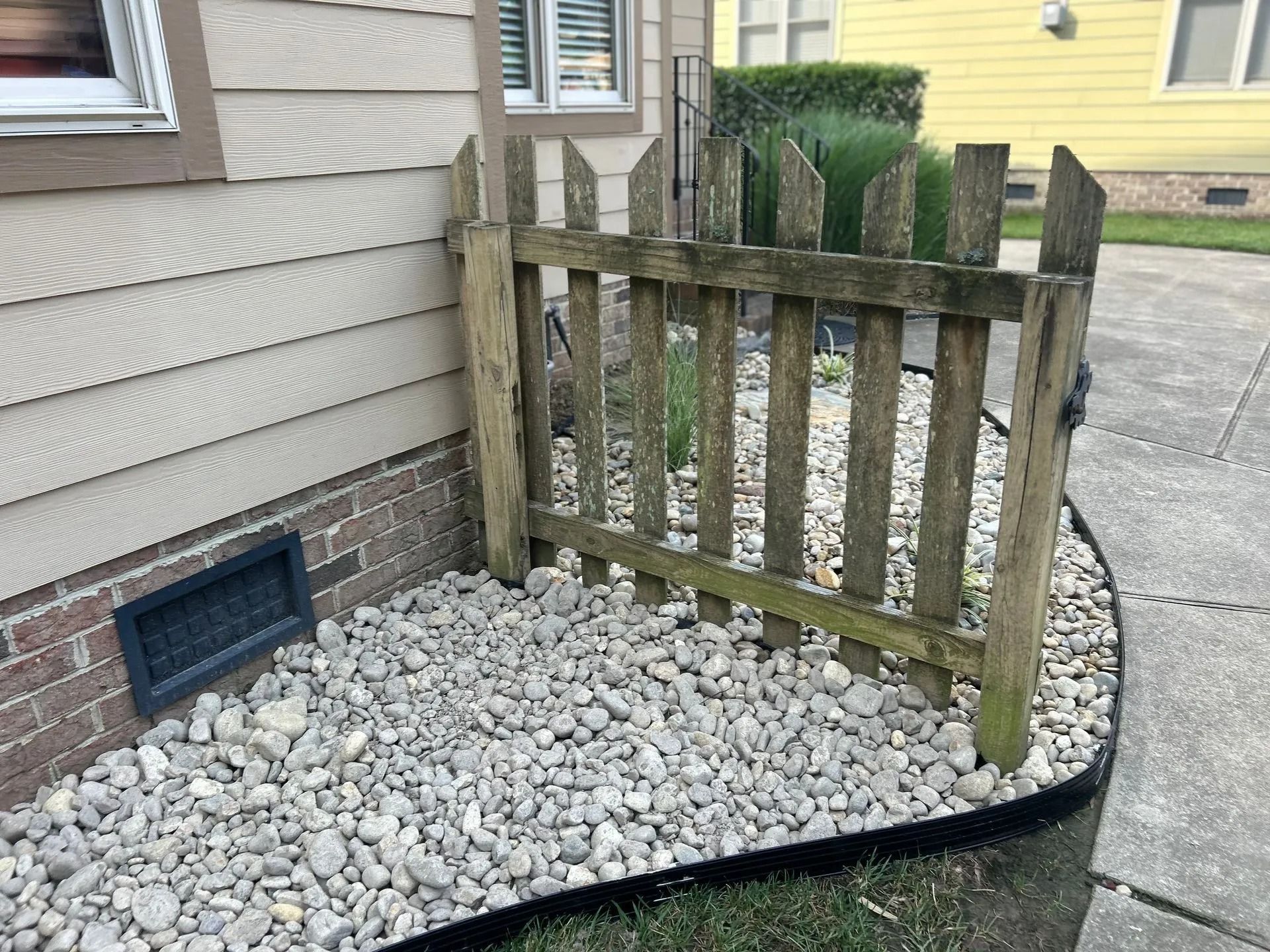 Wooden picket fence around gravel-filled area next to house.
