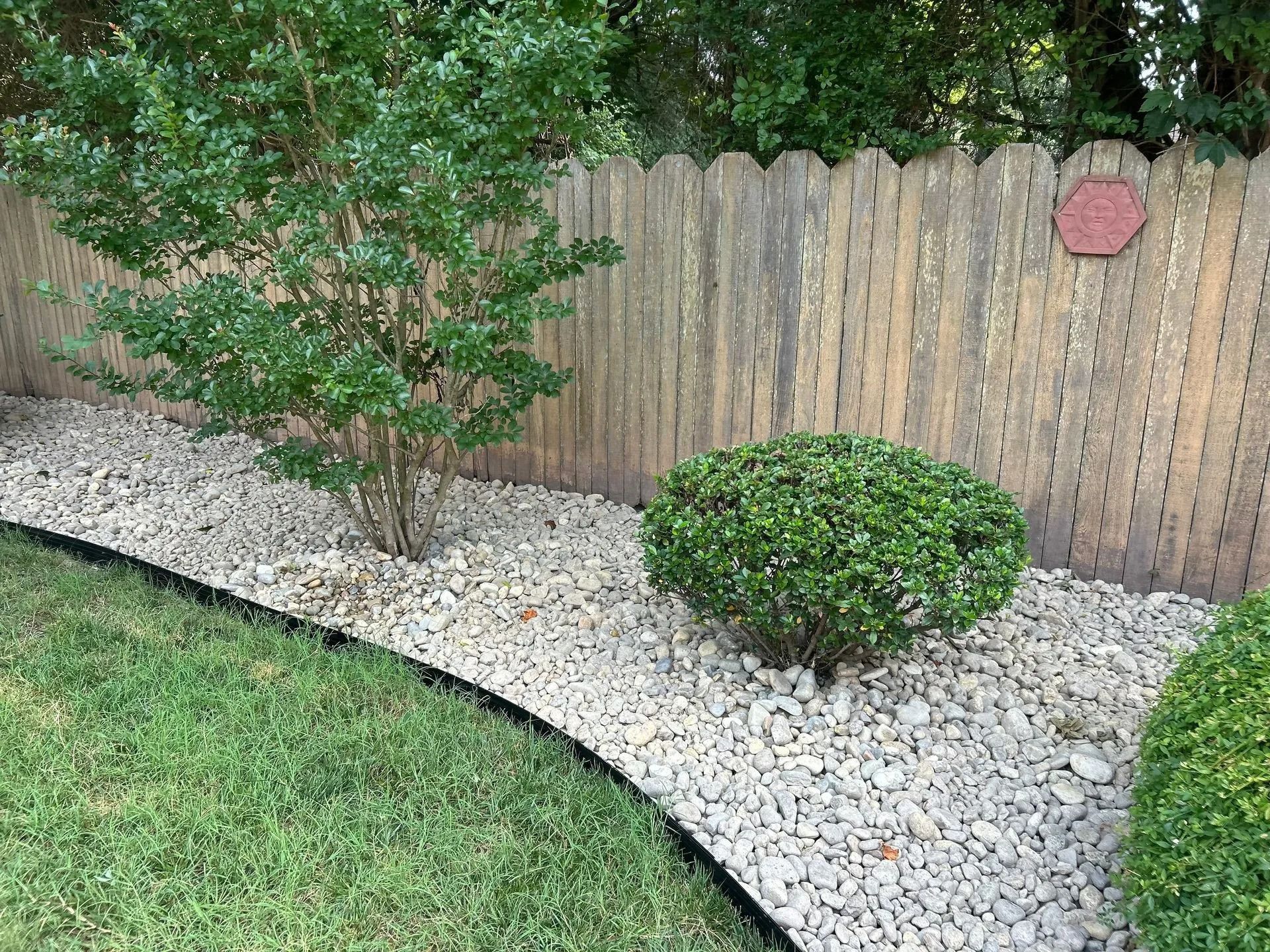 Landscaped yard with white rocks, green bushes, and a wooden fence.