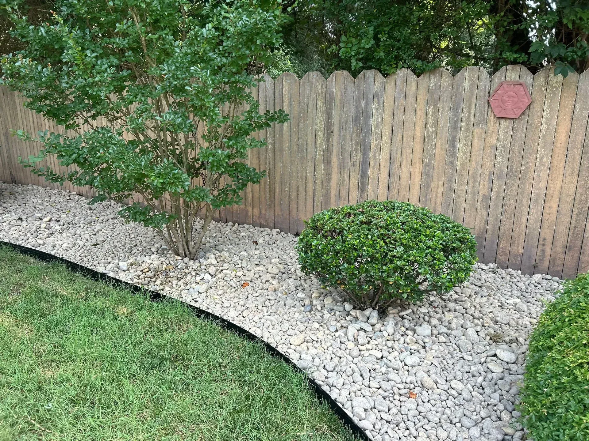 Gravel landscaping bed with green shrubs and a wooden fence.