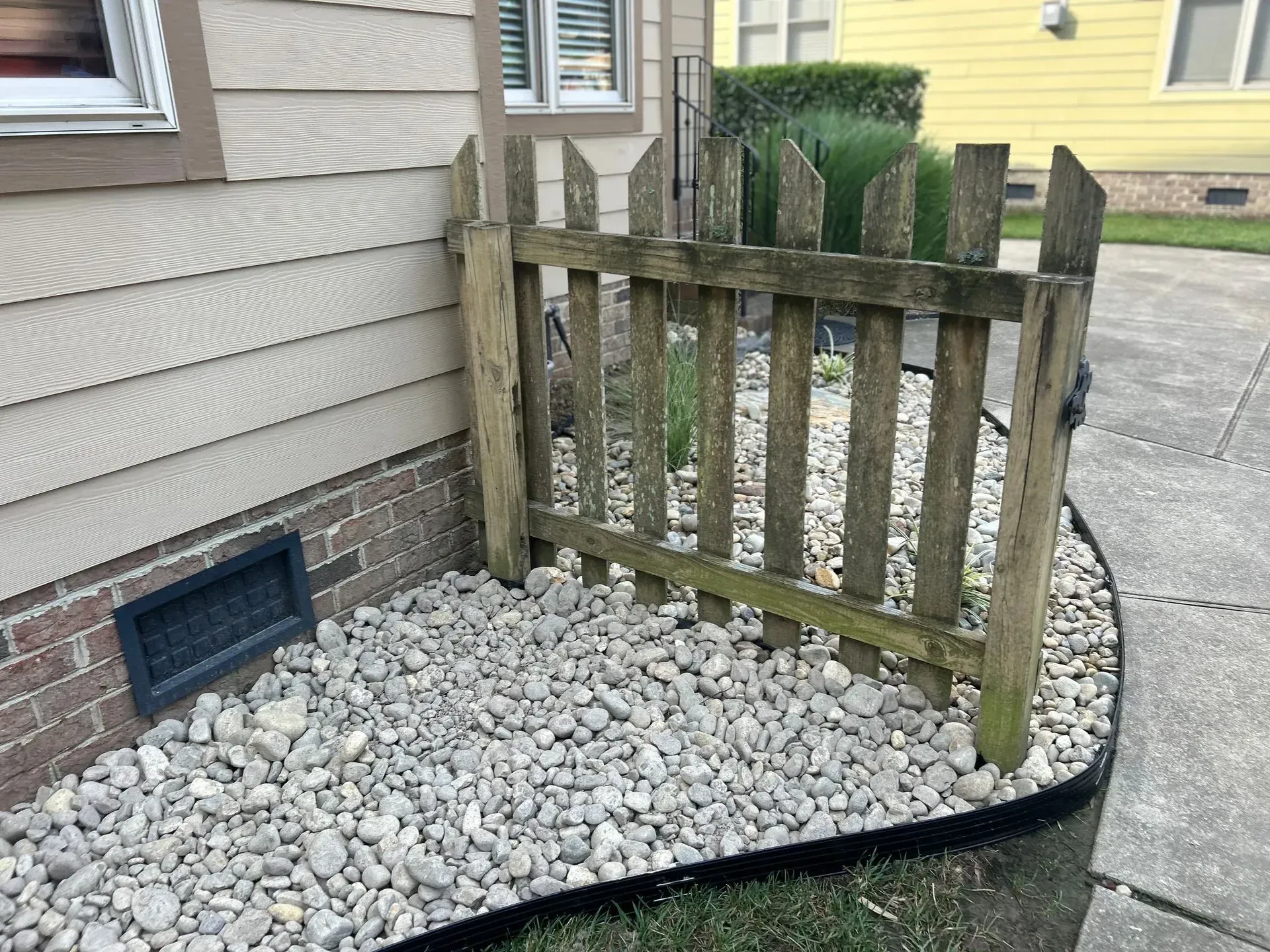 Small wooden fence in front of a house, surrounding gray gravel.