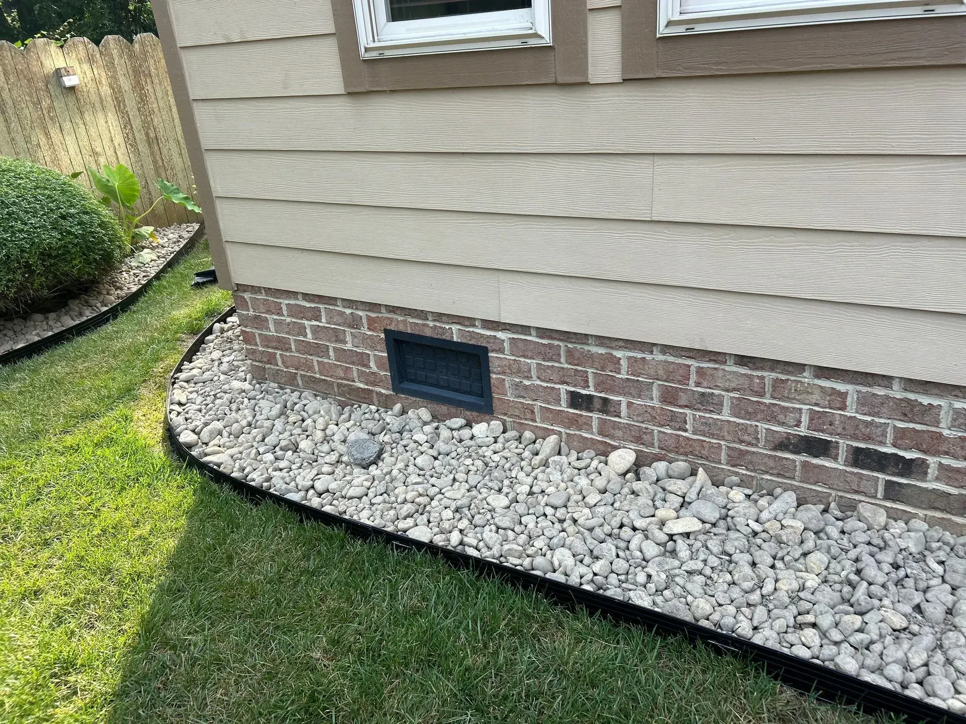 House exterior with brick foundation, beige siding, gray gravel landscaping, and black edging.