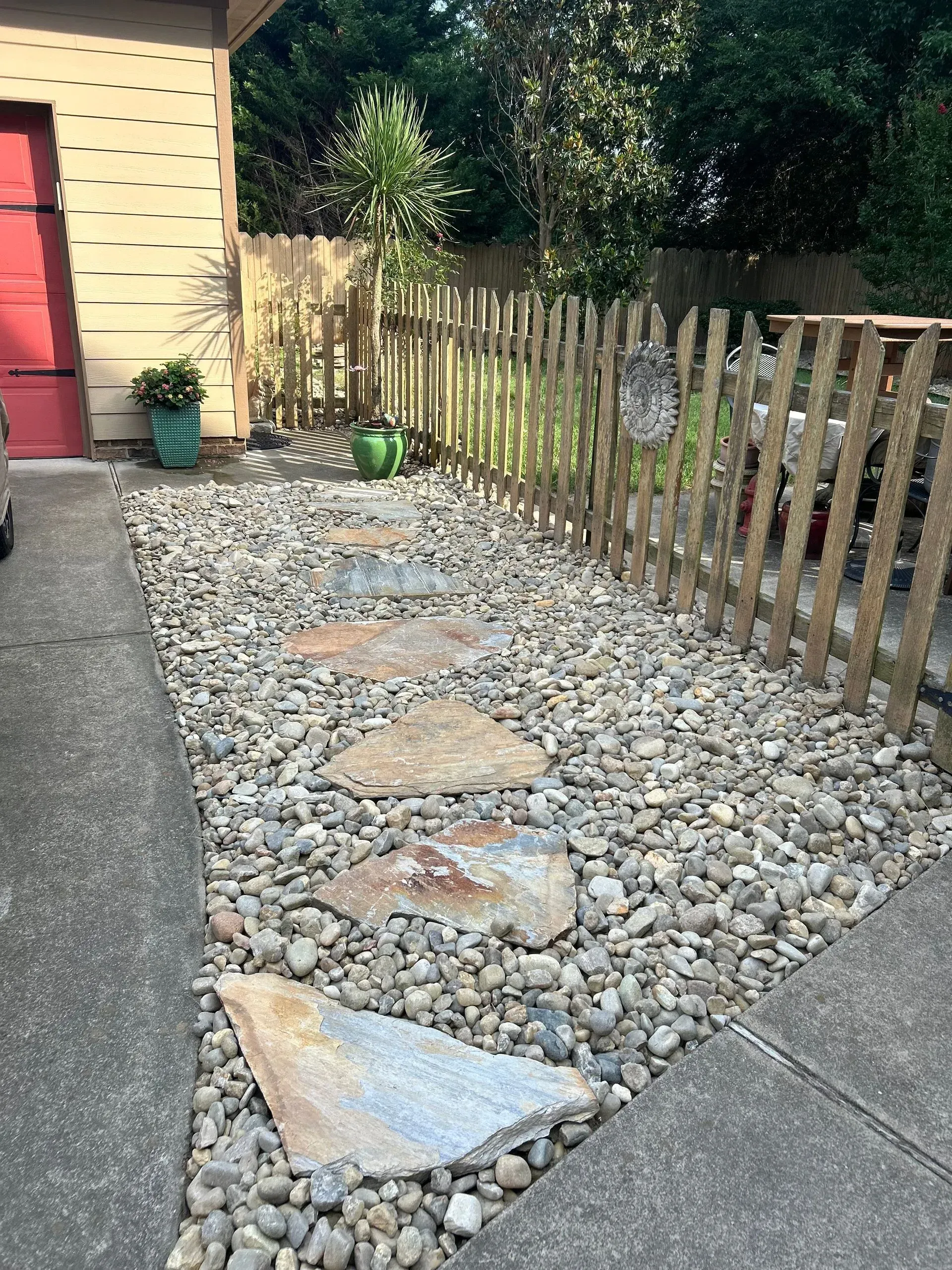 Pathway with stepping stones through a rock bed, bordered by a wooden fence and a garage.