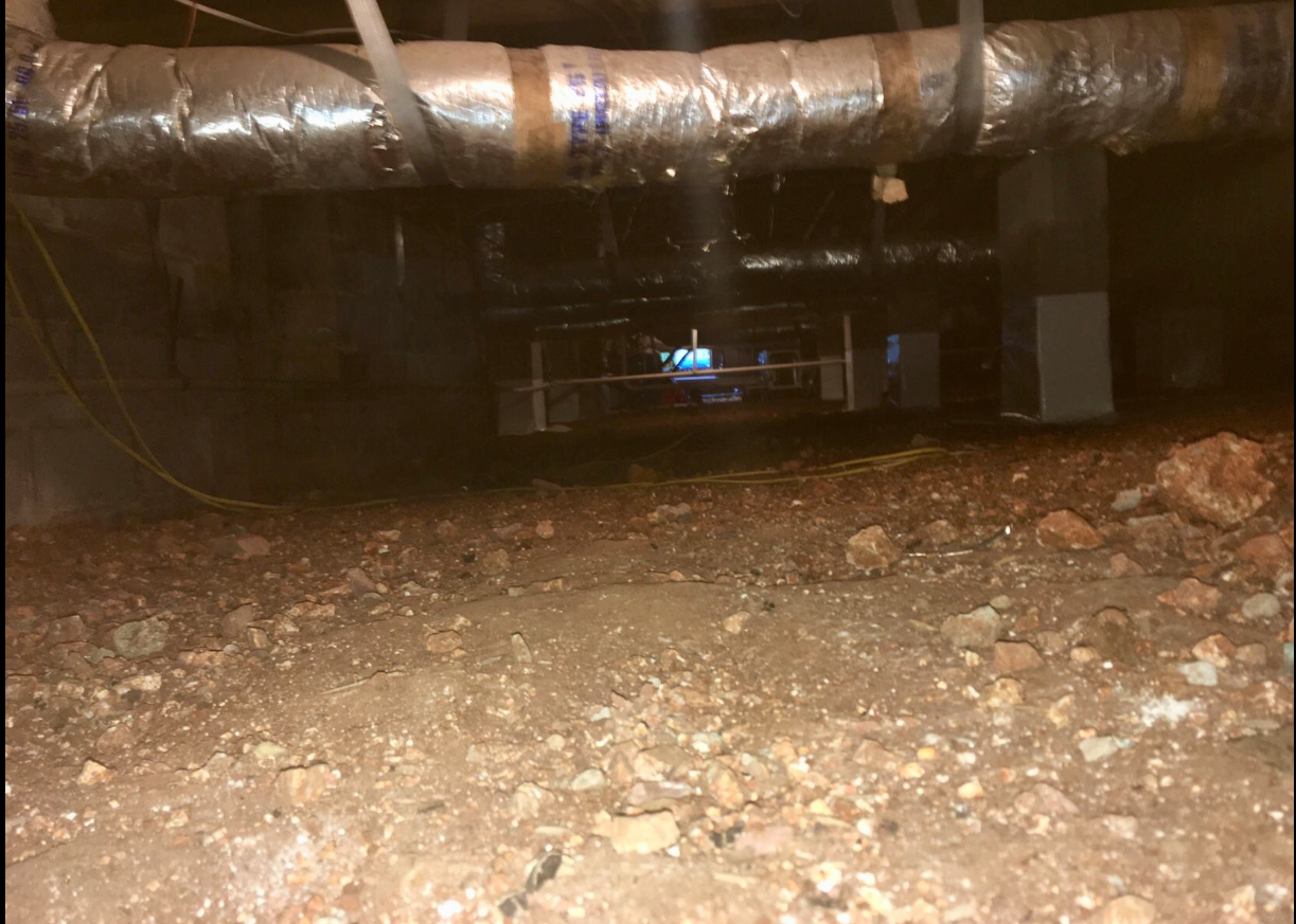 A dirty basement with a lot of pipes and rocks.