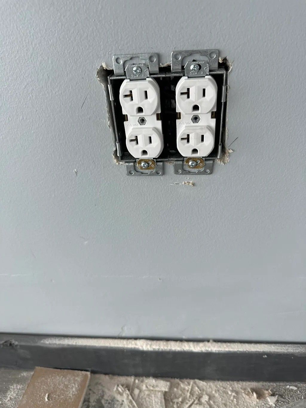 Two white electrical outlets mounted in a gray wall, screws visible.