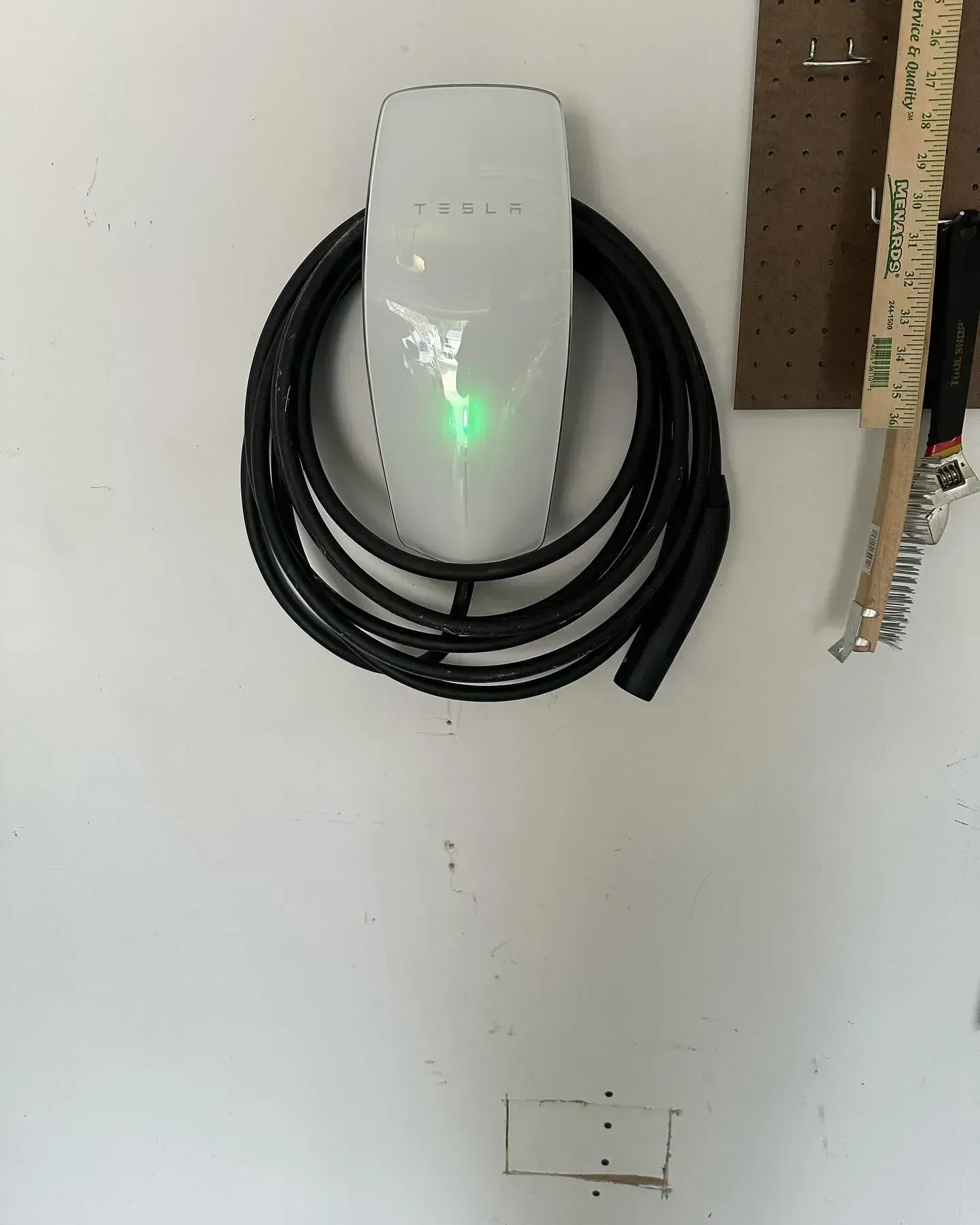Tesla charging station on a white wall with coiled black cable and green light
