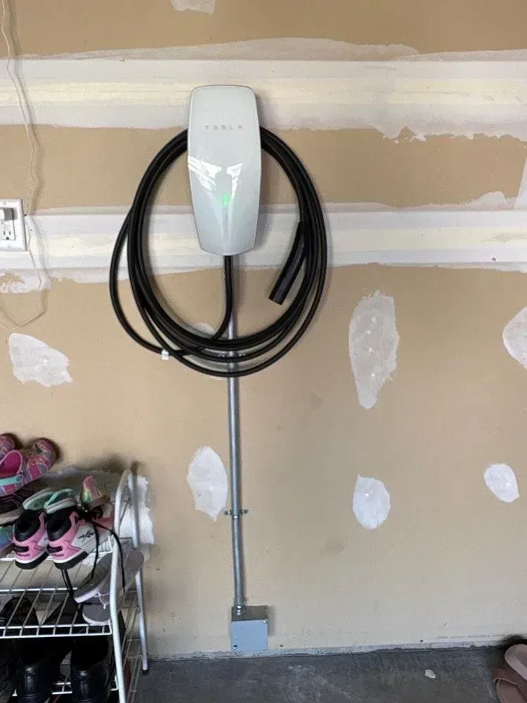 Tesla charging station mounted on a garage wall, with coiled cable and conduit