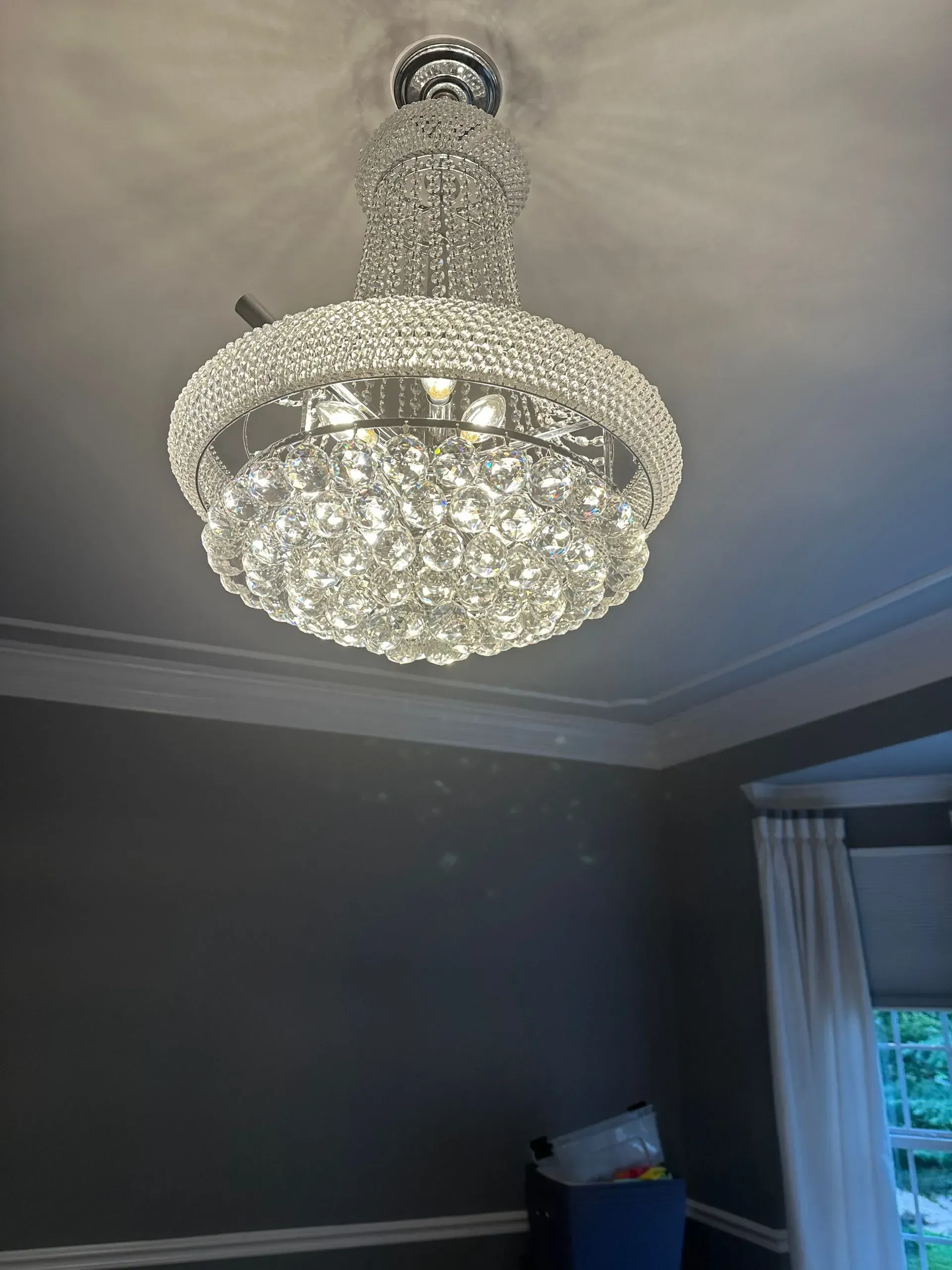 A large, ornate crystal chandelier hanging from a white ceiling in a room with gray walls