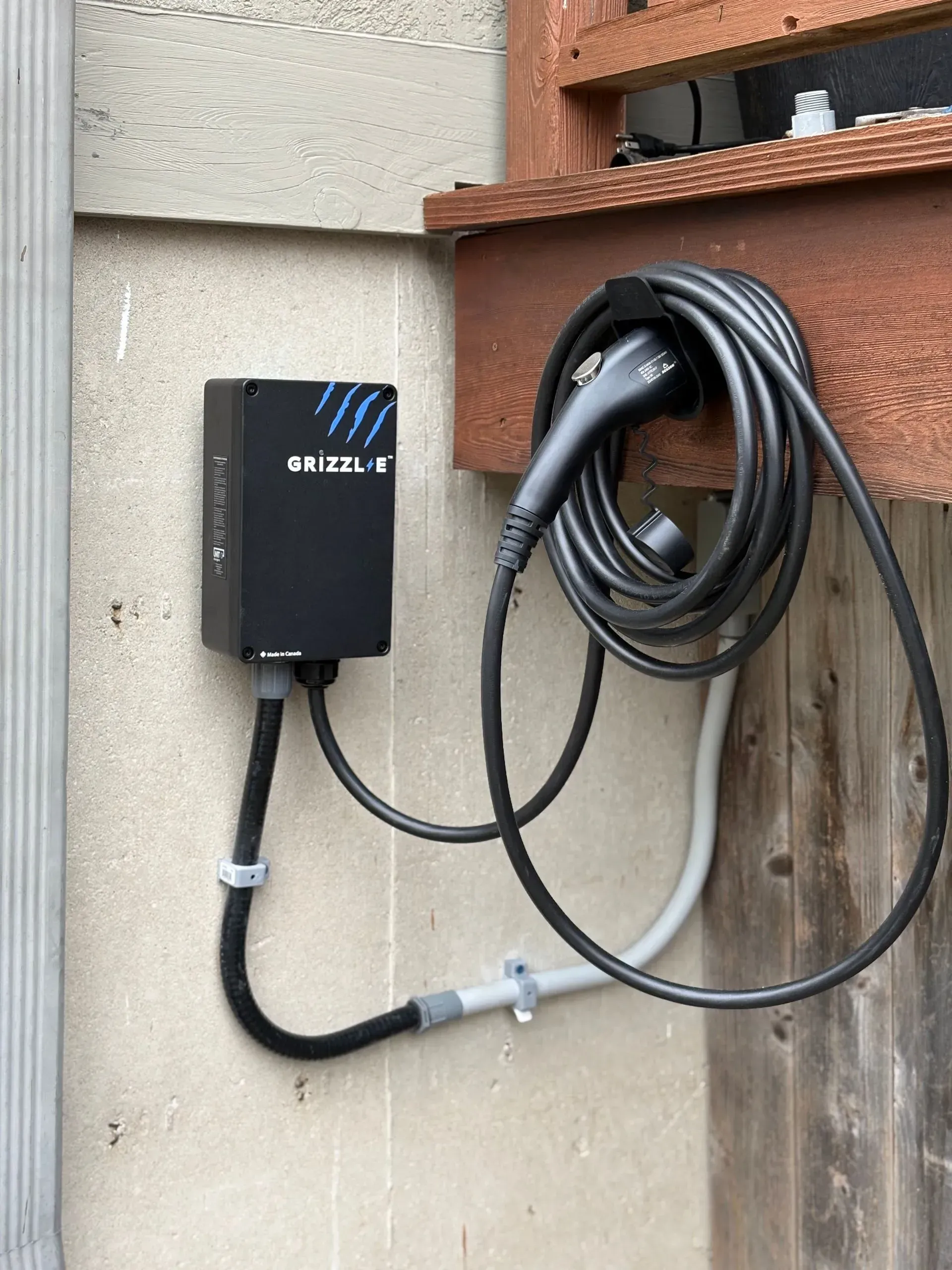 Black EV charger mounted on a stucco wall with coiled charging cable