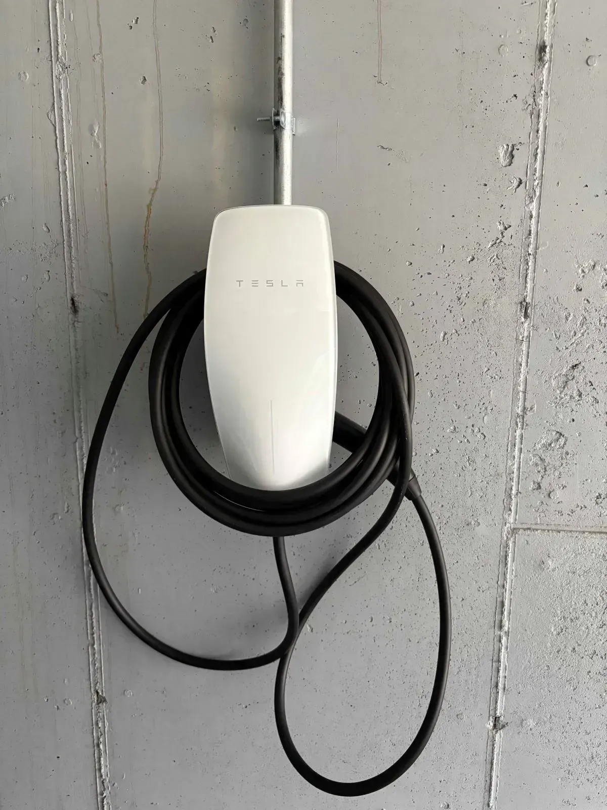 White Tesla charging station mounted on a grey concrete wall with black charging cable