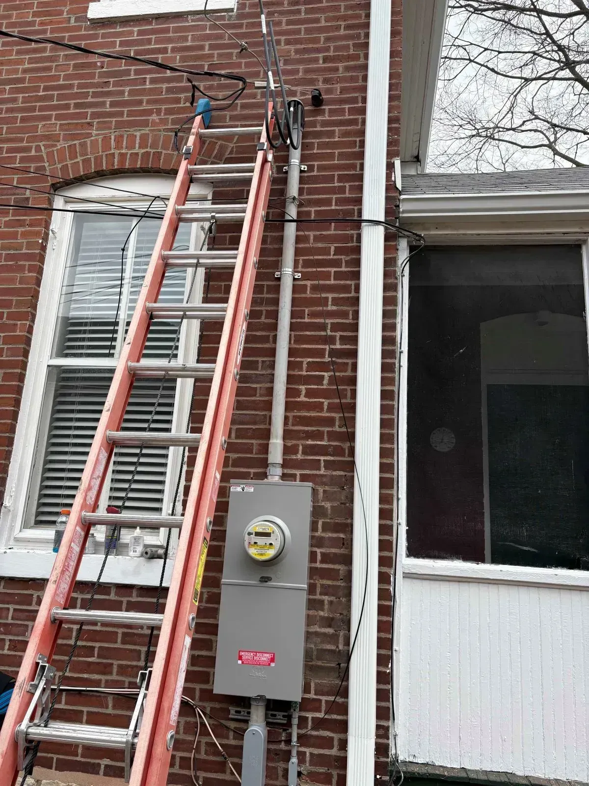 Ladder leans against a brick building near electrical equipment