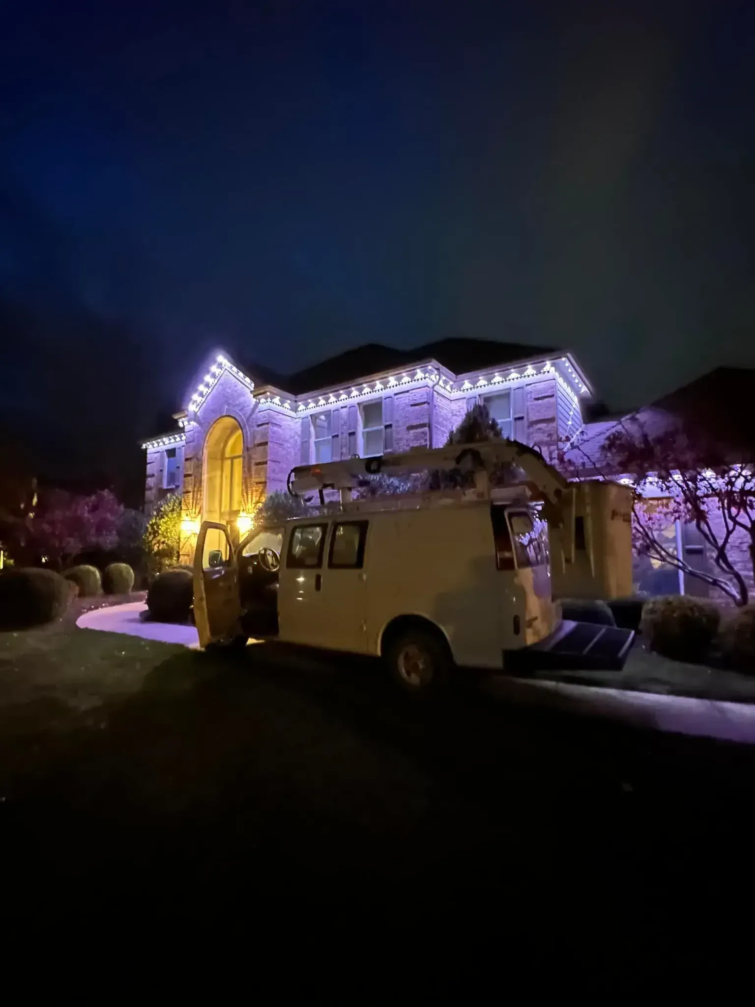White van parked in front of a house decorated with purple and white lights at night