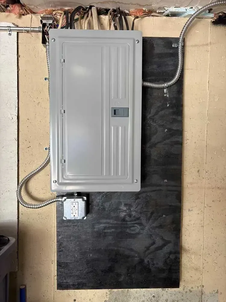 Electrical panel mounted on a dark board, with conduit and a junction box on a beige wall