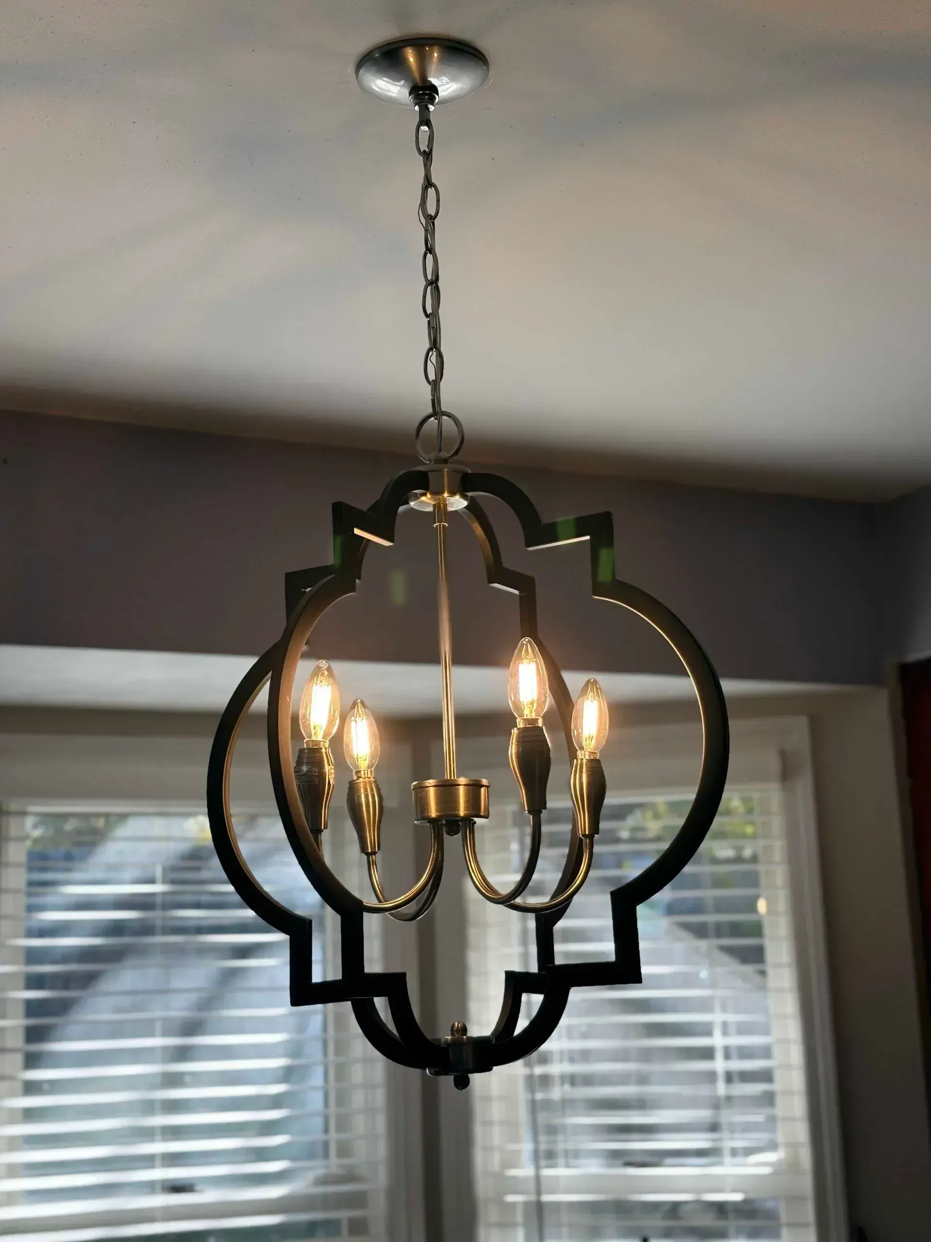 Gold and black ornate chandelier hanging from a ceiling, with lit bulbs inside