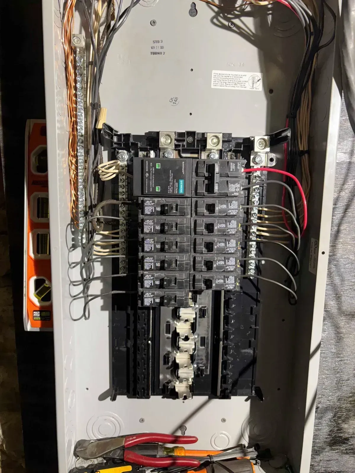 Open electrical panel with circuit breakers, wires, and tools