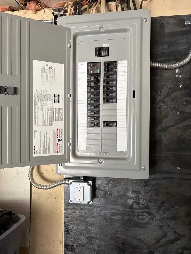 Open electrical panel with circuit breakers, mounted on a dark wall